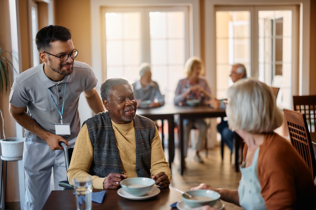 Happy senior people and their caregiver talking in dining room at at assisted living facility.