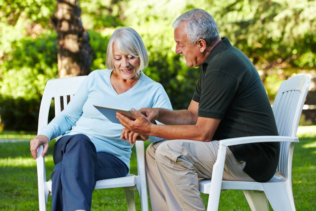 Two senior people sitting with a tablet PC in a nature park