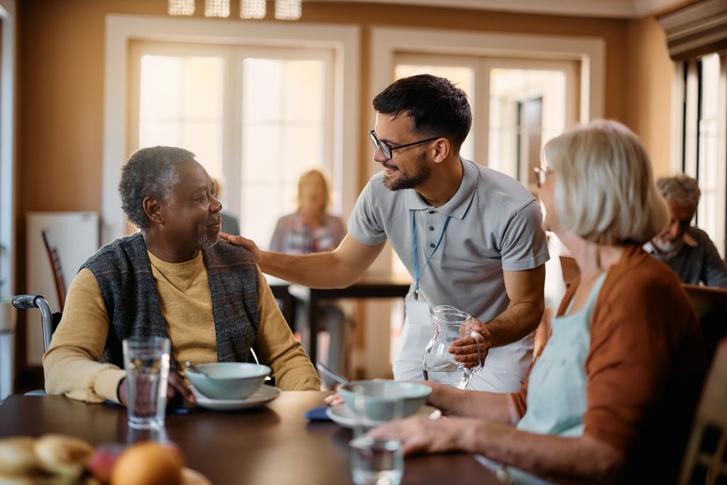 Young healthcare worker talking to seniors during lunch at assisted living home.