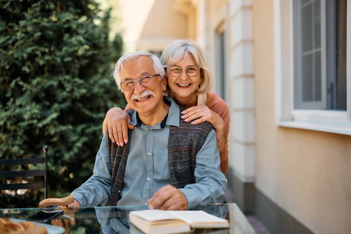 Happy senior couple spending time outside, reading books, smiling at the camera