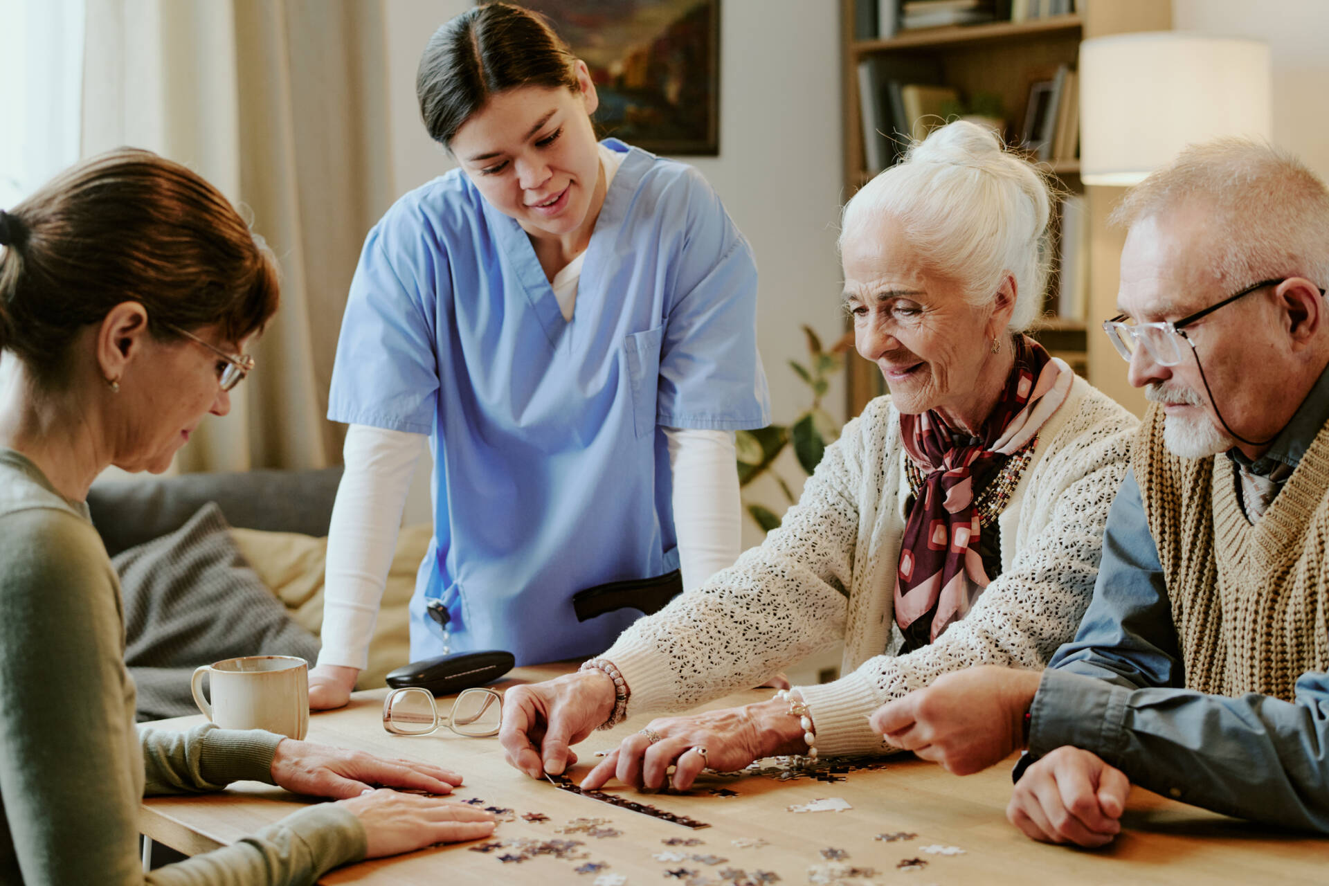 Senior Woman And Man Solving Puzzle With Nurse Assisting At Table